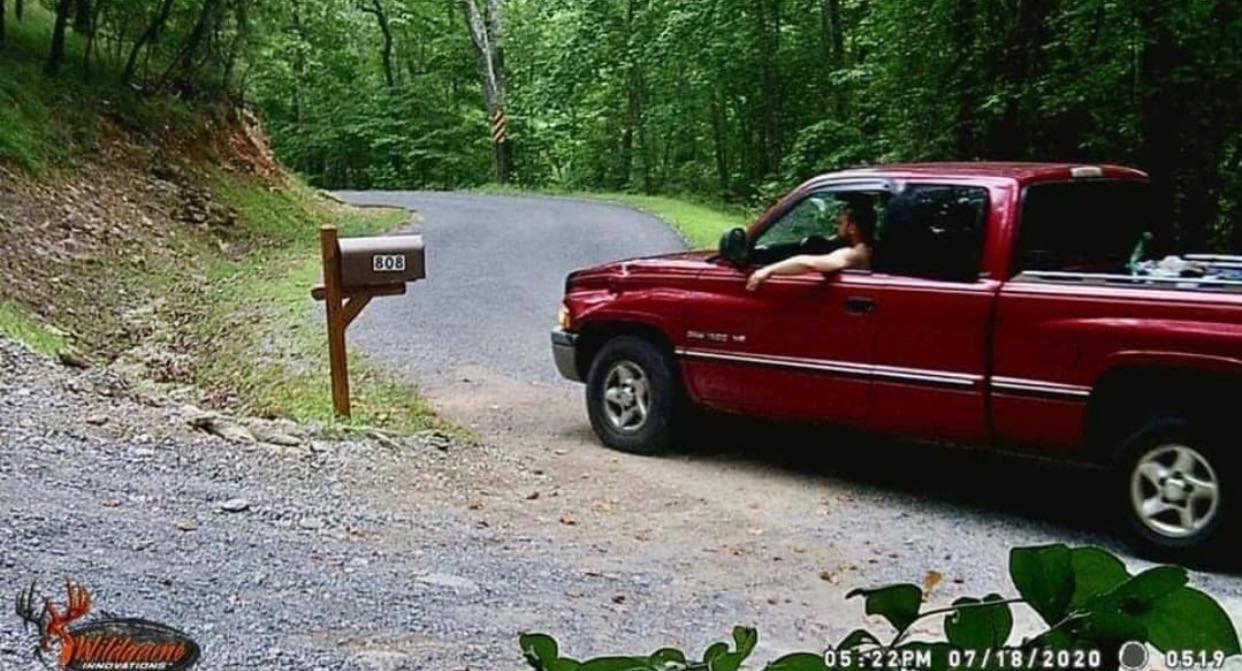 A maroon truck pulling up to a mailbox driven by a man